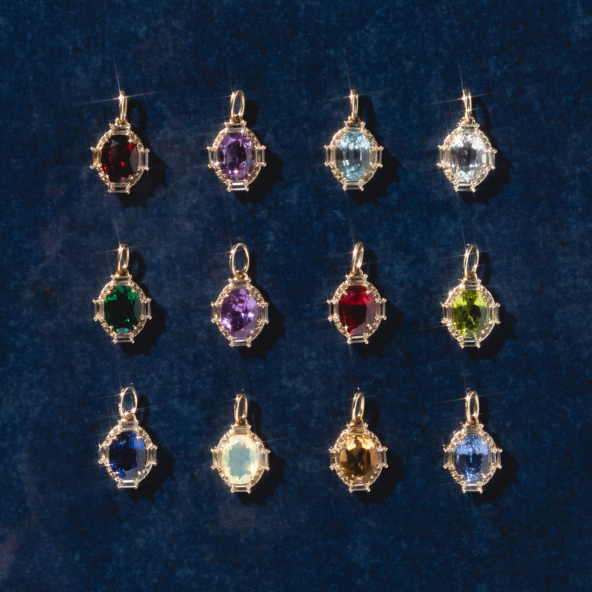 Twelve Solid Gold Vintage Inspired Birthstone Charms, each featuring a unique gemstone in a decorative gold frame, are arranged in a grid on a dark blue background.