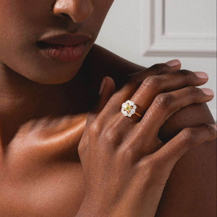 A woman with braided hair in a gray tank top glances to the side, her hand on her shoulder displaying the Floral Art Deco Inspired Peridot Ring.