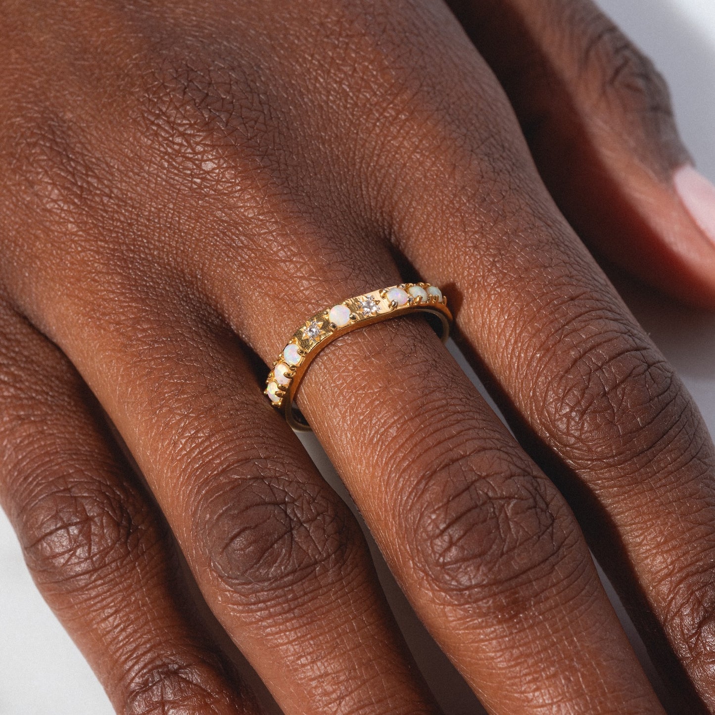 A close-up of a hand wearing the Opal Stacking Wave Ring, featuring small, sparkling gemstones on the ring finger against a light background.