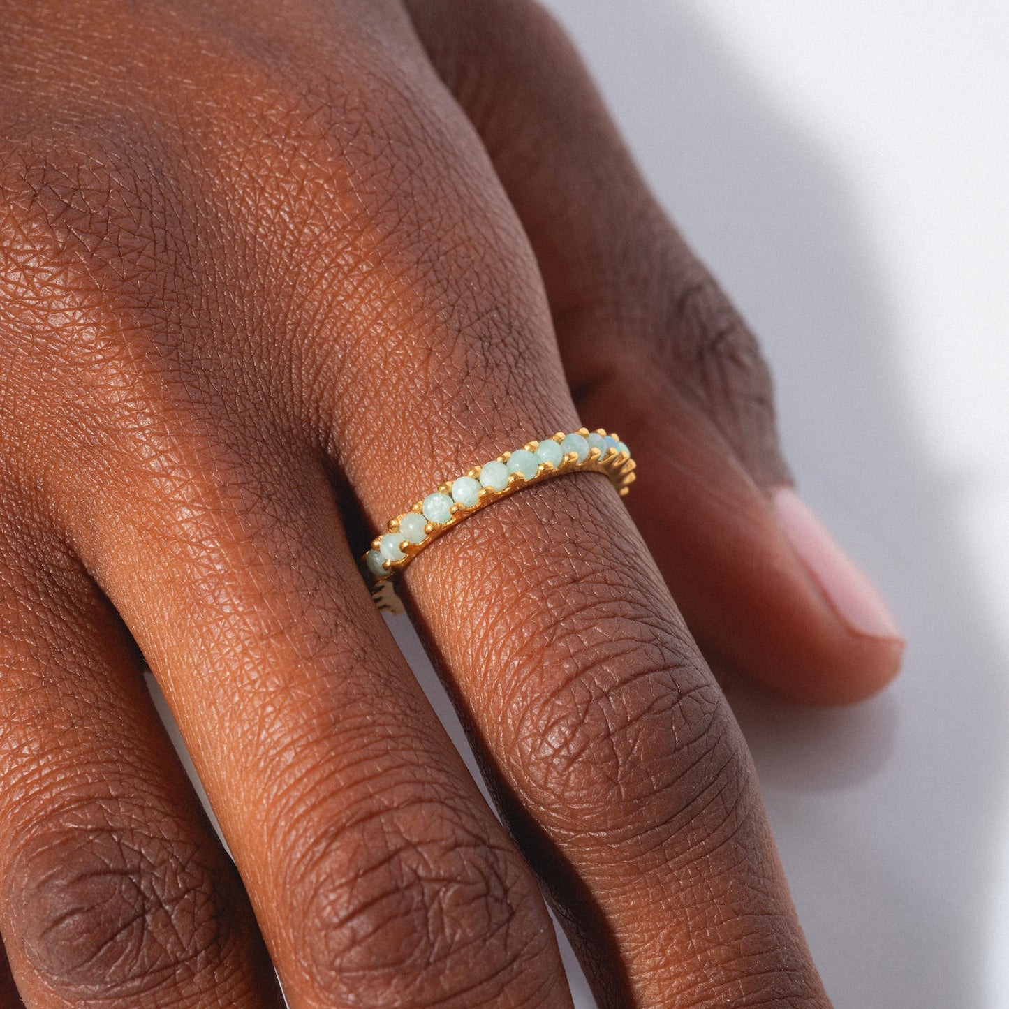 A close-up of a hand with neatly manicured nails wearing the Indecisive Opal and Amazonite Eternity Band in yellow gold vermeil, featuring small, round opal and amazonite stones on the ring finger.