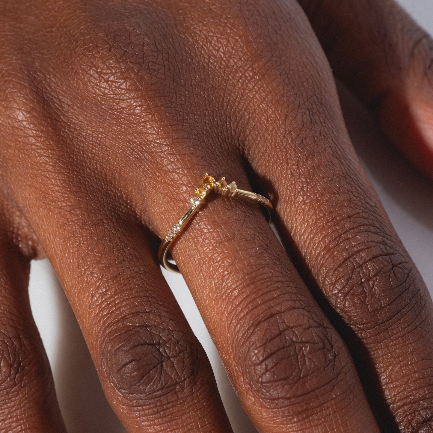 A close-up shows a hand wearing the Solid Gold 2025 November Capsule Delicate Arch Citrine Stacking Ring, featuring delicate details, displayed on a finger against a neutral background.