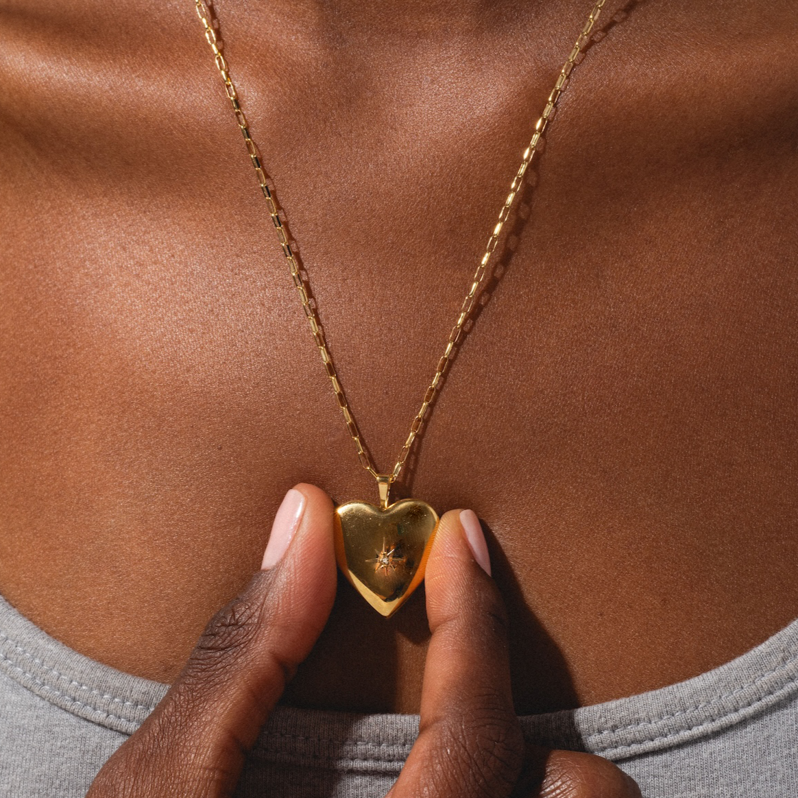 Gold heart-shaped necklace being held by a hand against a brown background