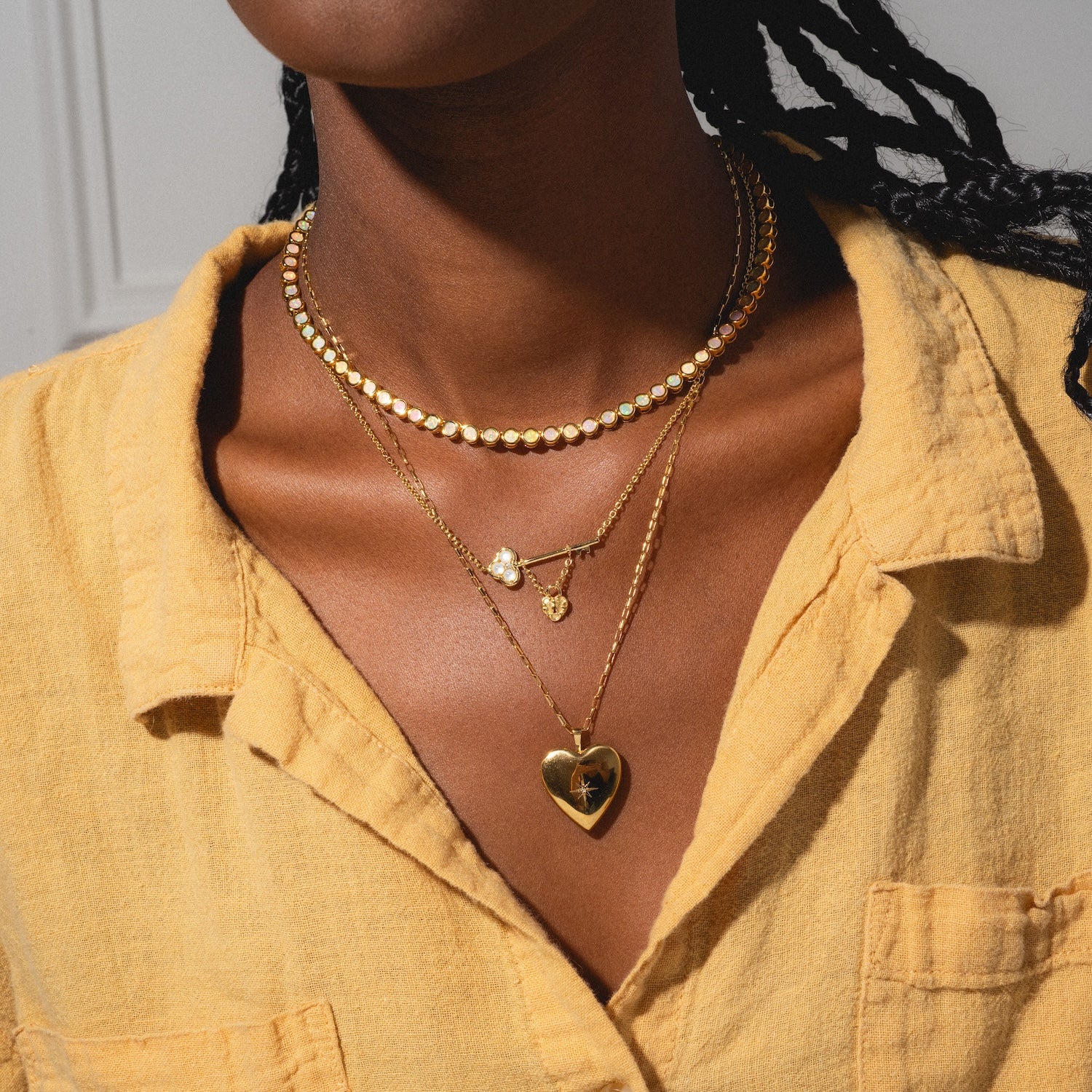 Person wearing multiple gold necklaces with a mustard yellow shirt.