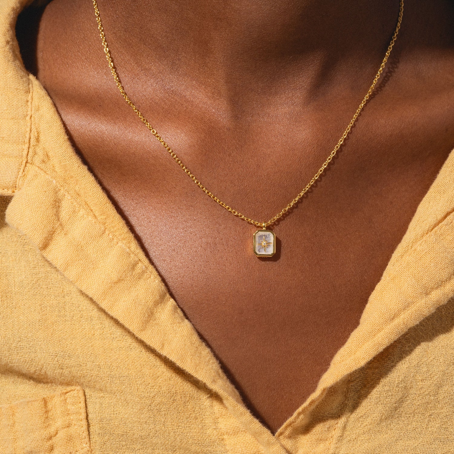 A close-up of a person wearing the Rainbow Moonstone & Diamond Manifest Your Dreams Pendant Necklace paired with a yellow collared shirt.