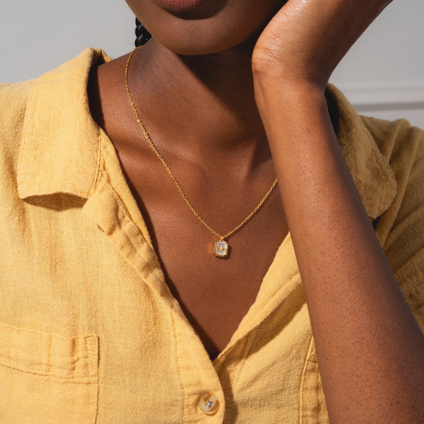 A woman in a textured yellow shirt showcases the Rainbow Moonstone & Diamond Manifest Your Dreams Pendant Necklace, featuring a rectangular pendant. The focus is on her jewelry and shirt, with her face partially out of frame.