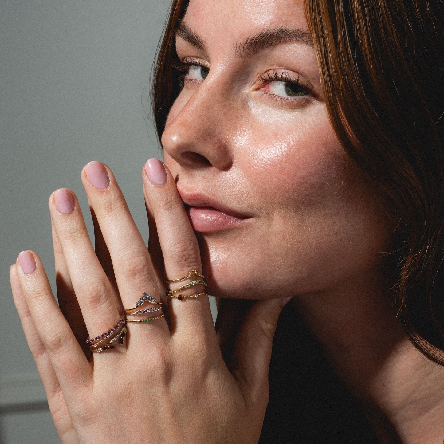A woman with natural makeup and a confident smile showcases the Solid Gold 2025 February Capsule Garnet Full Set on her fingers, highlighting multiple gold rings with garnet accents.