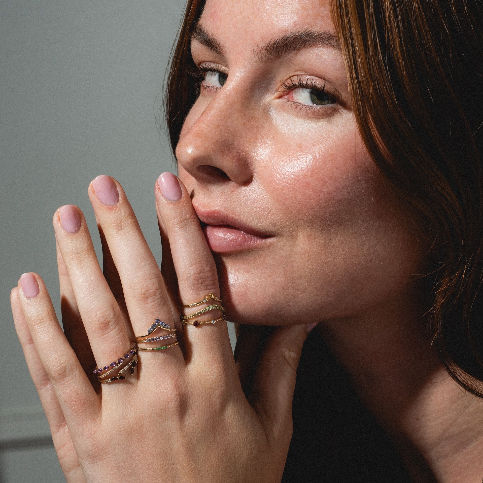 A woman with natural makeup and a confident smile showcases the Solid Gold 2025 February Capsule Garnet Full Set on her fingers, highlighting multiple gold rings with garnet accents.