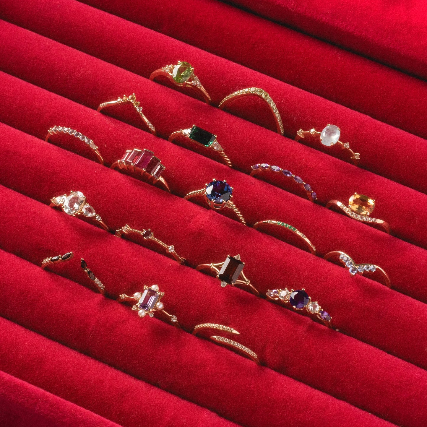 A Solid Gold 2025 February Capsule Garnet Full Set with free gift, featuring assorted gold rings with colorful gemstones and unique designs, is displayed on red velvet in neat rows.