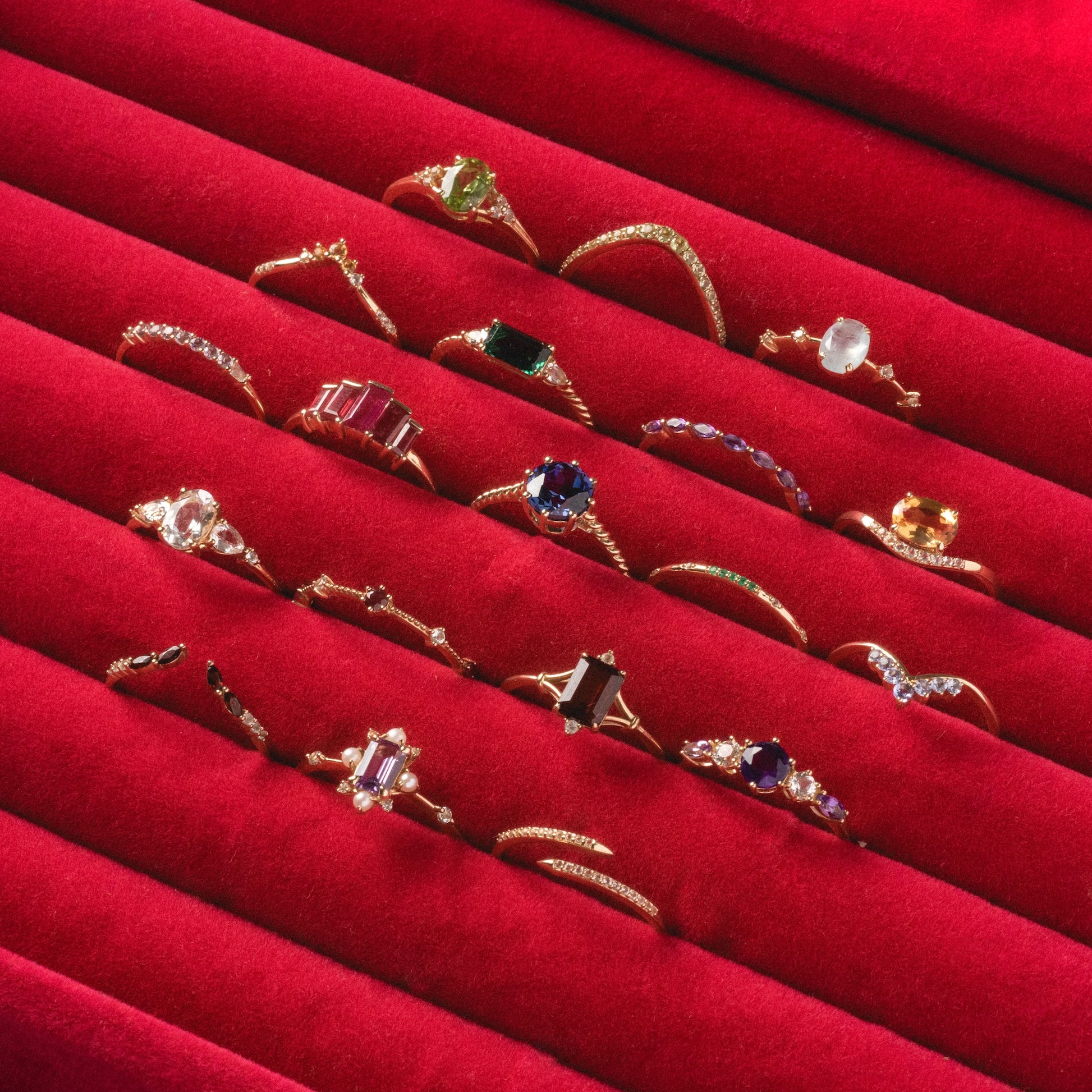 A Solid Gold 2025 February Capsule Garnet Full Set with free gift, featuring assorted gold rings with colorful gemstones and unique designs, is displayed on red velvet in neat rows.