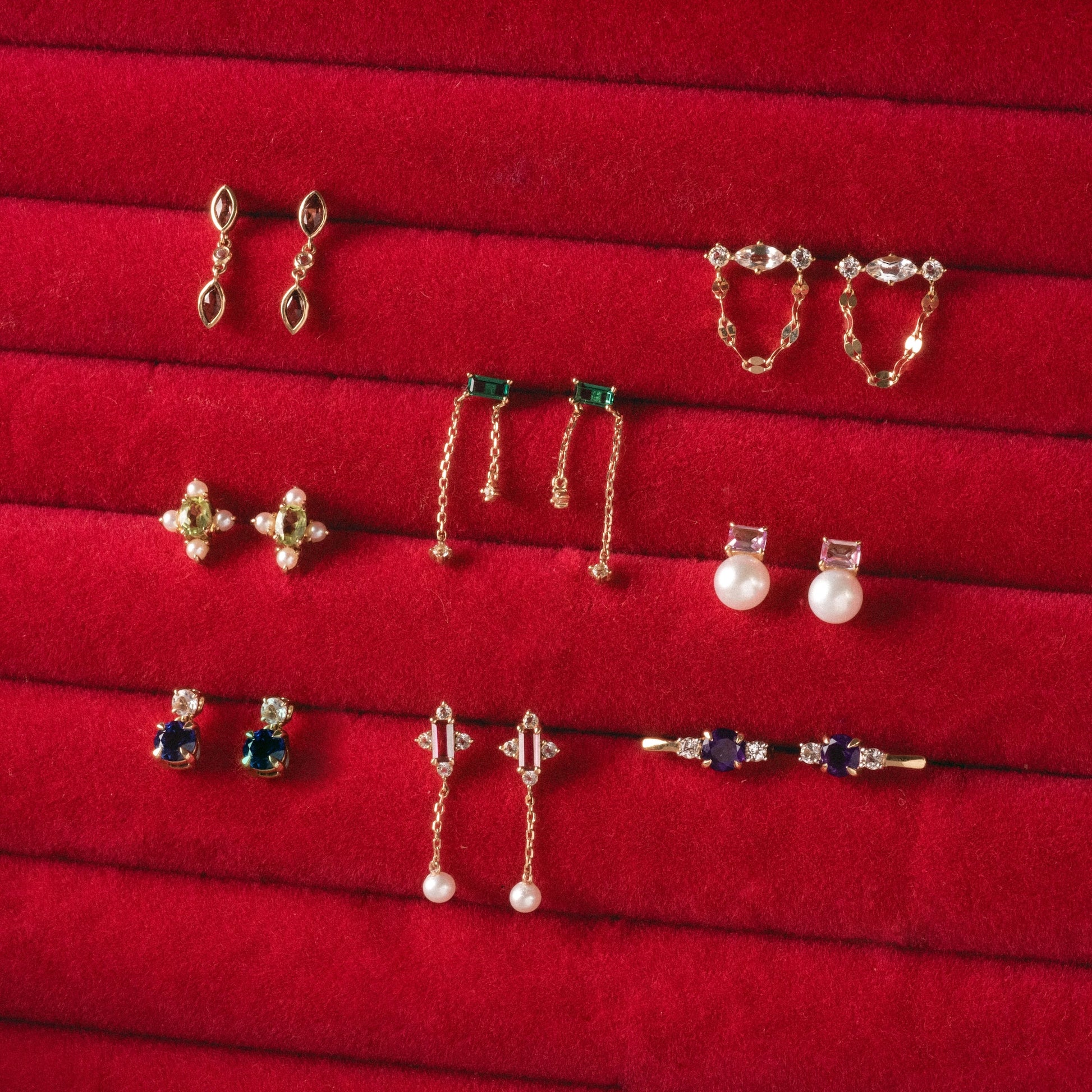 Nine pairs from the Solid Gold 2025 February Capsule Garnet Full Set, featuring gold, pearl, gemstone, and diamond styles with unique details, are beautifully arranged on a red velvet display. Free gift included.