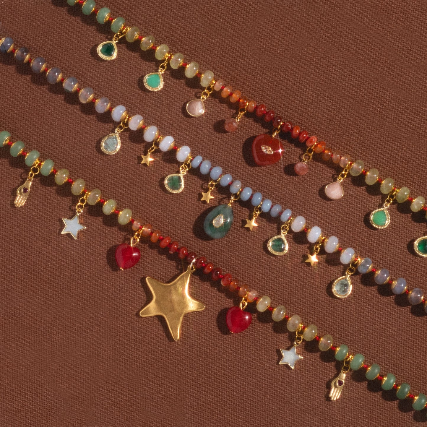 The True North Necklace features colorful beads and various dangling gold charms—stars, hamsa hands, teardrop gems, and heart-shaped pendants—beautifully displayed on a brown surface.
