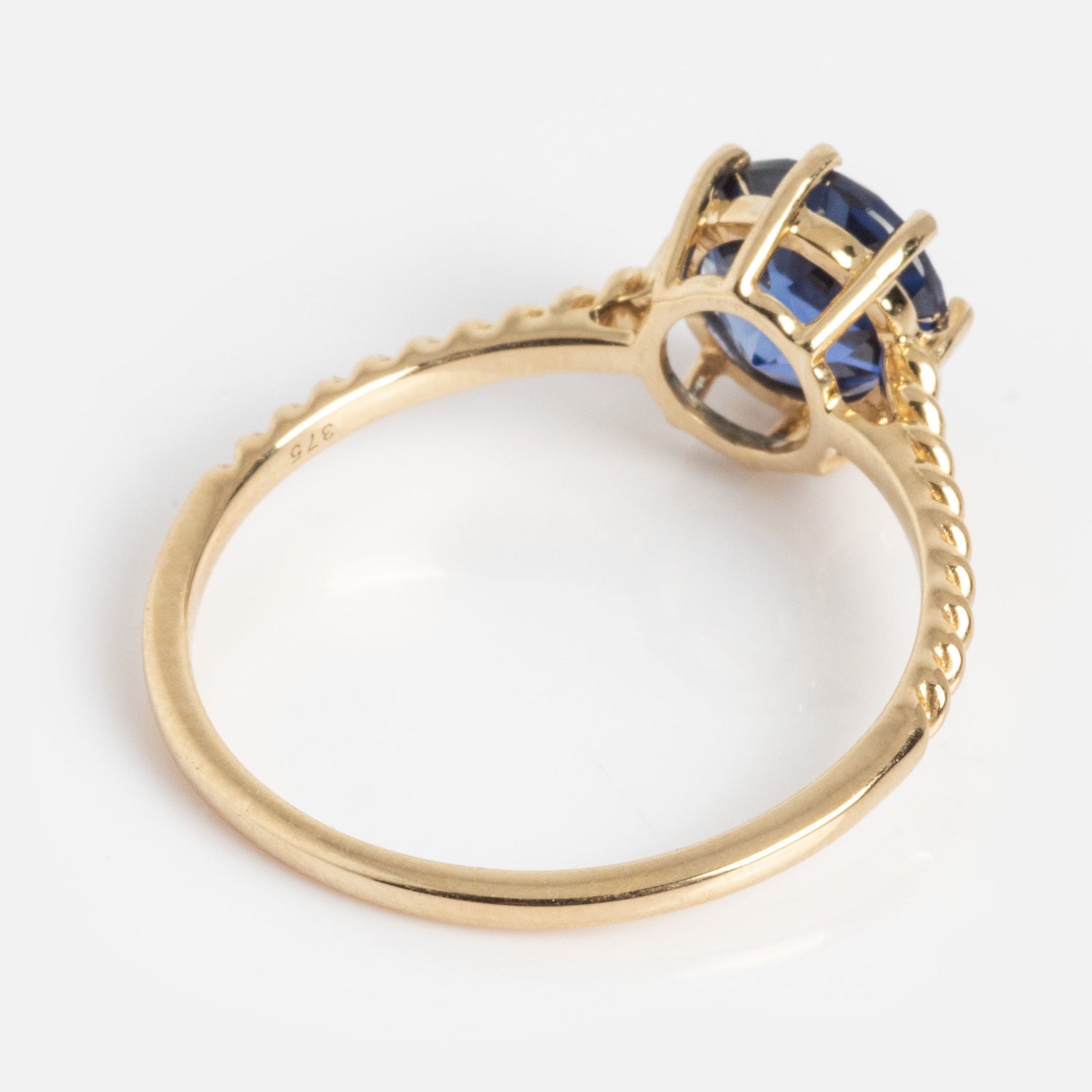 The Solid Gold 2025 December Capsule Classic Tanzanite Statement Ring features a twisted gold band and a large blue tanzanite gemstone in a prong setting, shown from the side against a plain white background.
