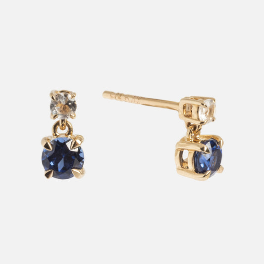 A pair of Solid Gold 2025 December Capsule Classic Tanzanite Stud Earrings, each with a small clear stone above a larger round blue tanzanite in prong settings, shown against a plain white background.