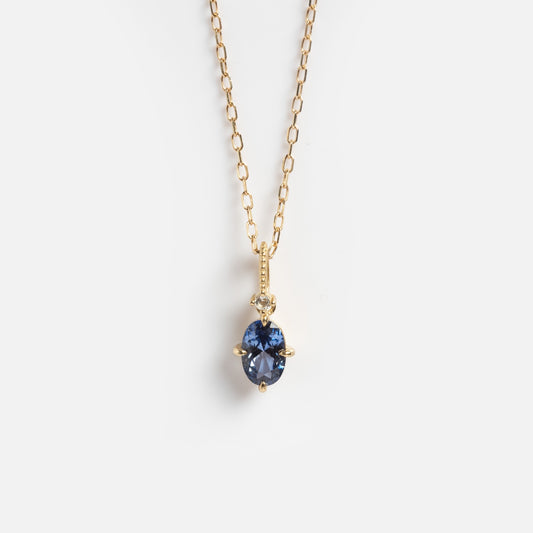 The Solid Gold 2025 December Capsule Classic Tanzanite Pendant Necklace features an oval blue tanzanite pendant with a small round diamond above it, displayed on a plain white background.