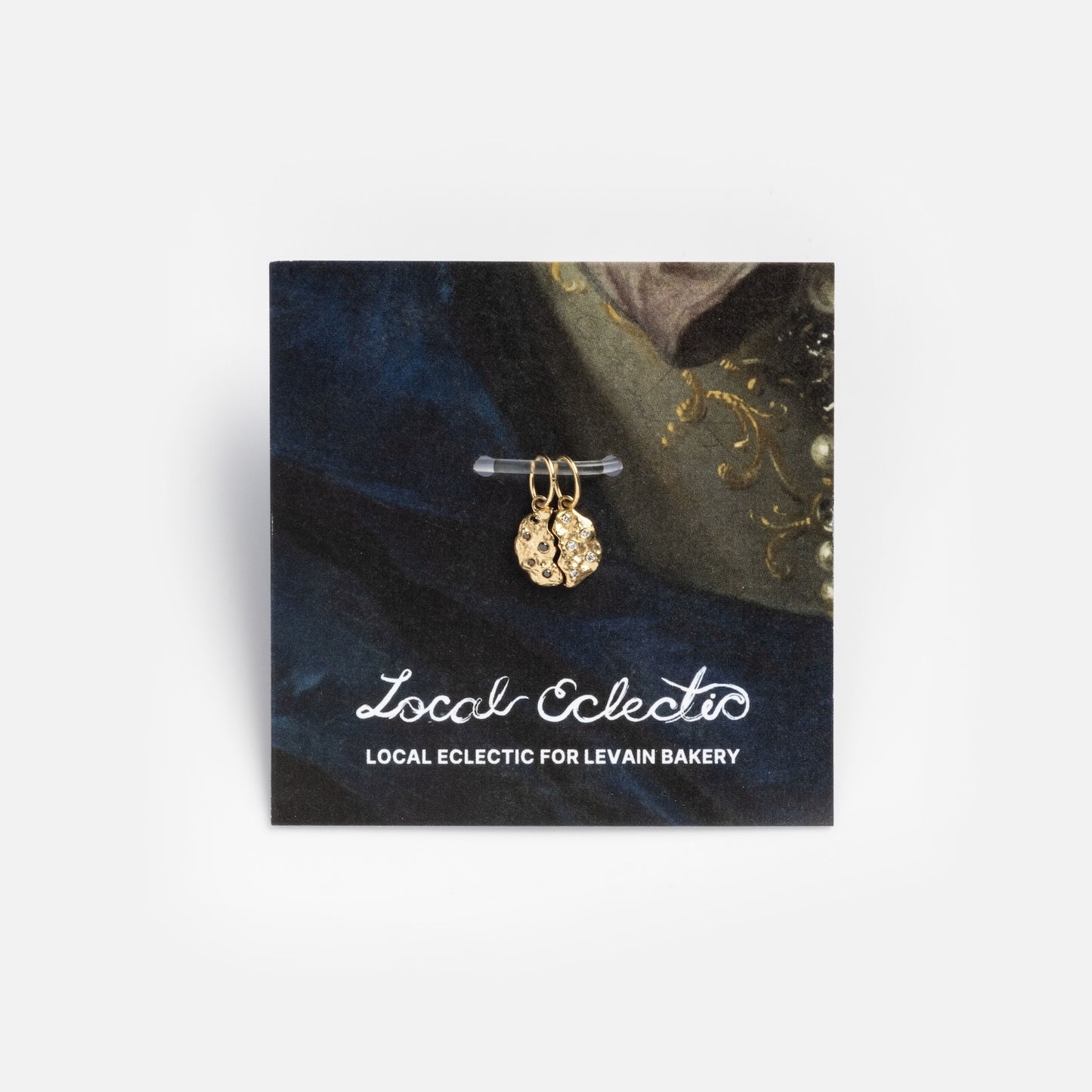 The Levain Bakery x Local Eclectic Solid Gold Share a Cookie Friendship Charm is shown on a card with “Local Eclectic for Levain Bakery” text, set against a stylish blue and green background.