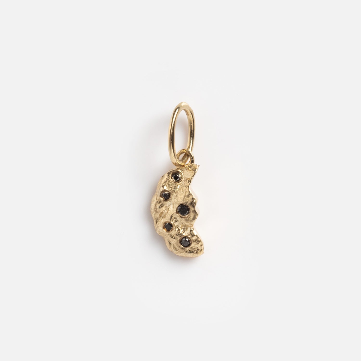 The Levain Bakery x Local Eclectic Solid Gold Share a Cookie Friendship Charm features a small, irregularly shaped gold pendant with a textured surface and embedded dark gemstones, hanging from a simple gold loop.