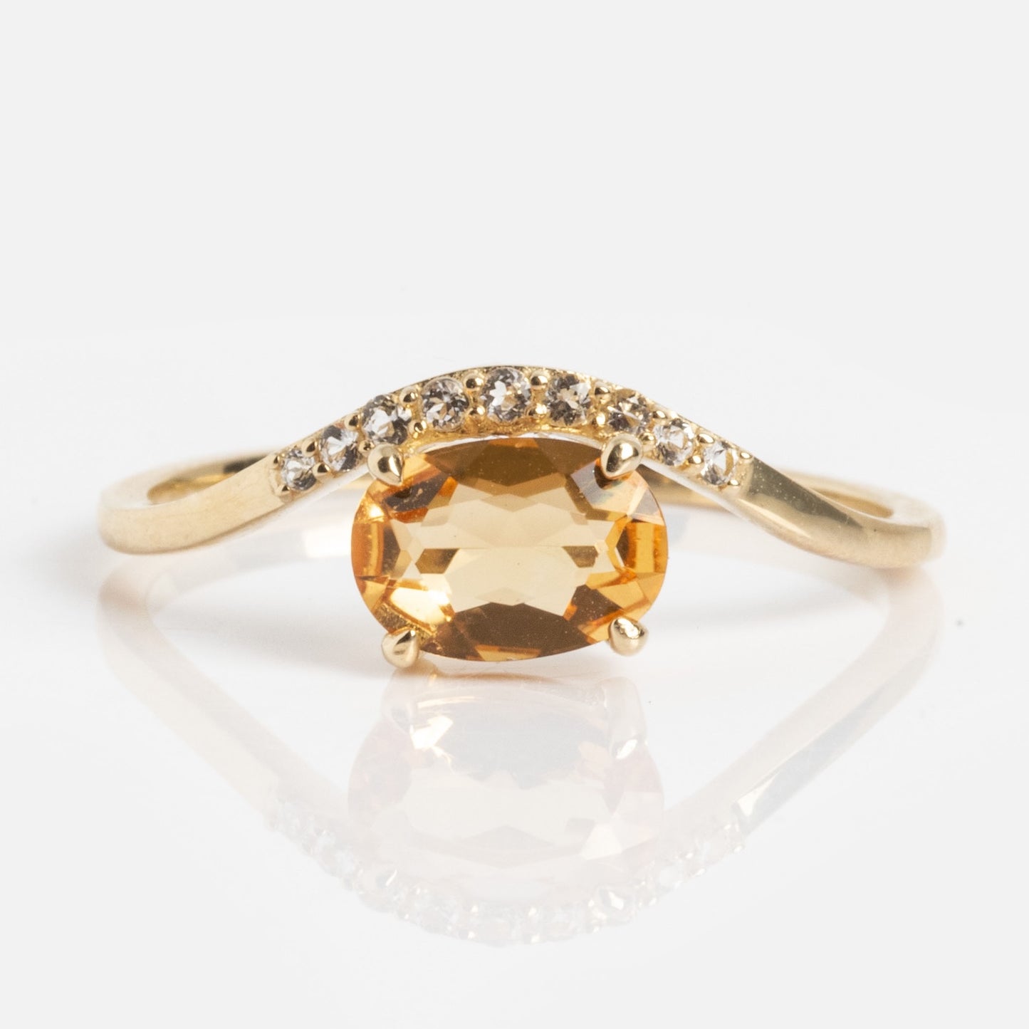 The Solid Gold 2025 November Capsule Floating Citrine Statement Ring features an oval citrine center, accented by small clear stones on one side of the band, showcased on a white background.