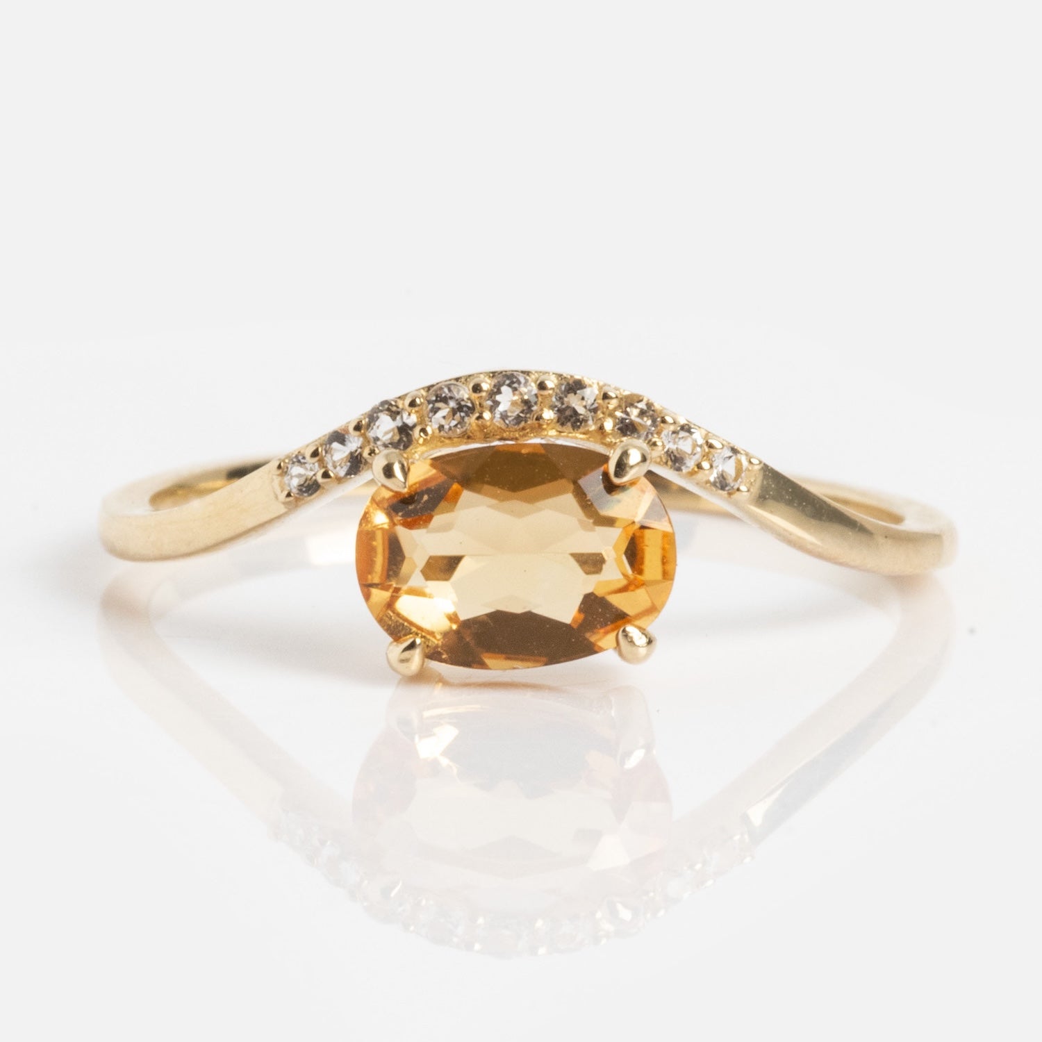 The Solid Gold 2025 November Capsule Floating Citrine Statement Ring features an oval citrine center, accented by small clear stones on one side of the band, showcased on a white background.