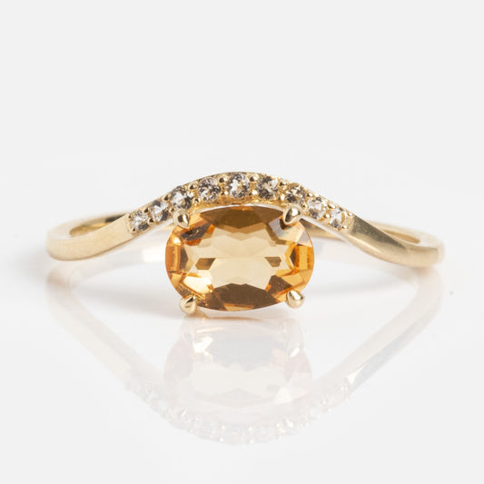 The Solid Gold 2025 November Capsule Floating Citrine Statement Ring features an oval citrine center, accented by small clear stones on one side of the band, showcased on a white background.