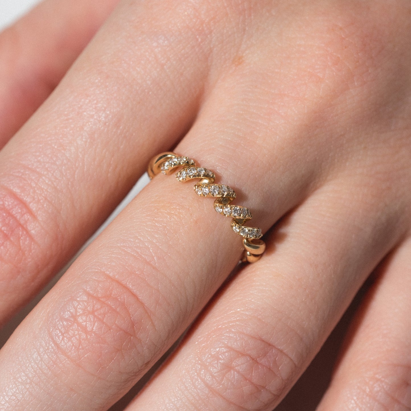 A close-up of a hand wearing the 14k Fated Twist Diamond Ring—a gold ring with a twisted design and small diamonds set along the top, shown on the middle finger.