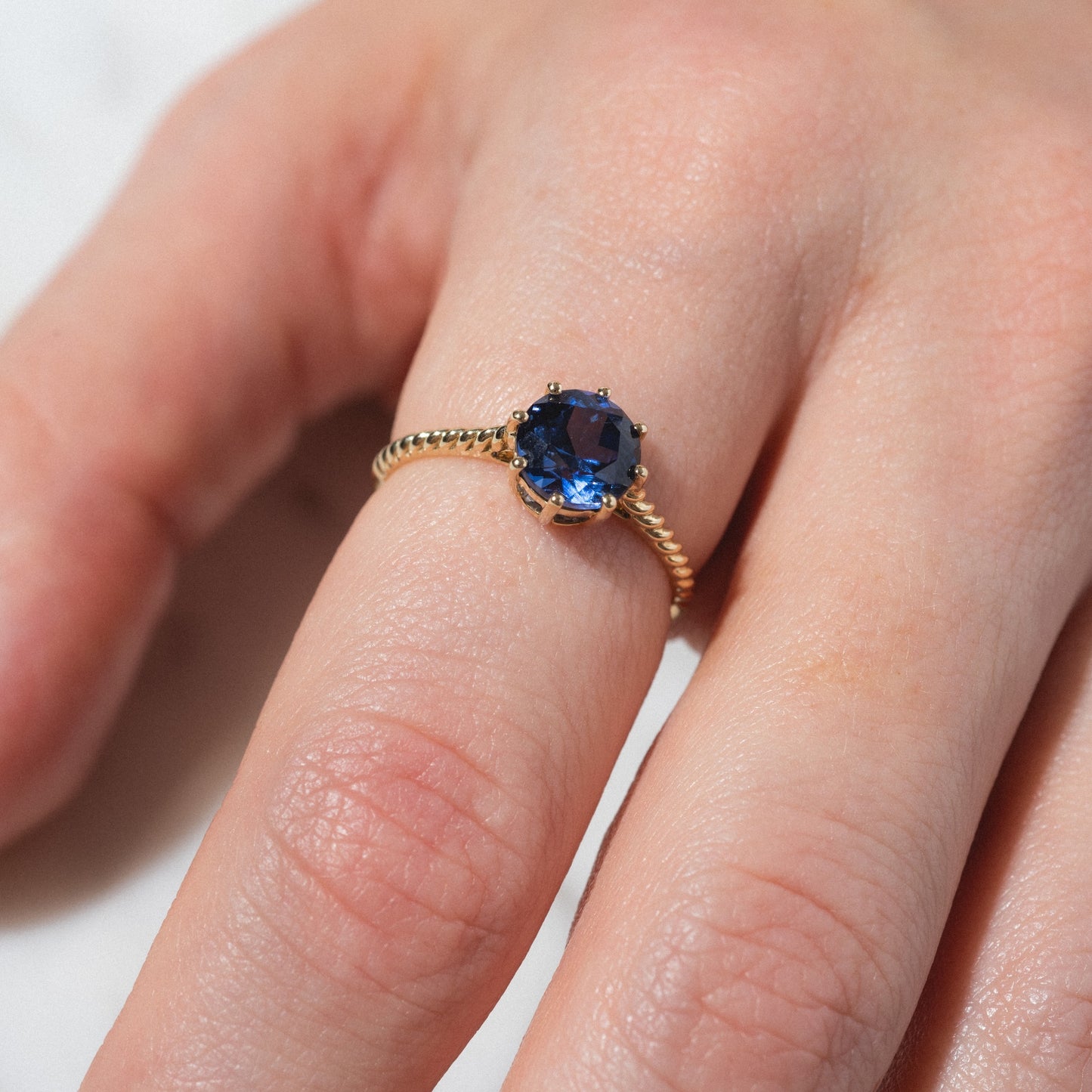 A close-up of a hand wearing the Solid Gold 2025 December Capsule Classic Tanzanite Statement Ring, featuring a round deep blue tanzanite set in a decorative gold band on the ring finger.