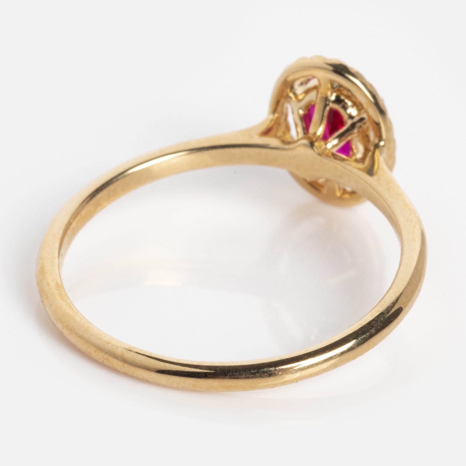 The 10k Lucky In Red Ruby Halo Ring features a thin gold band with an ornate side profile, highlighting intricate red ruby details in its elegant setting.
