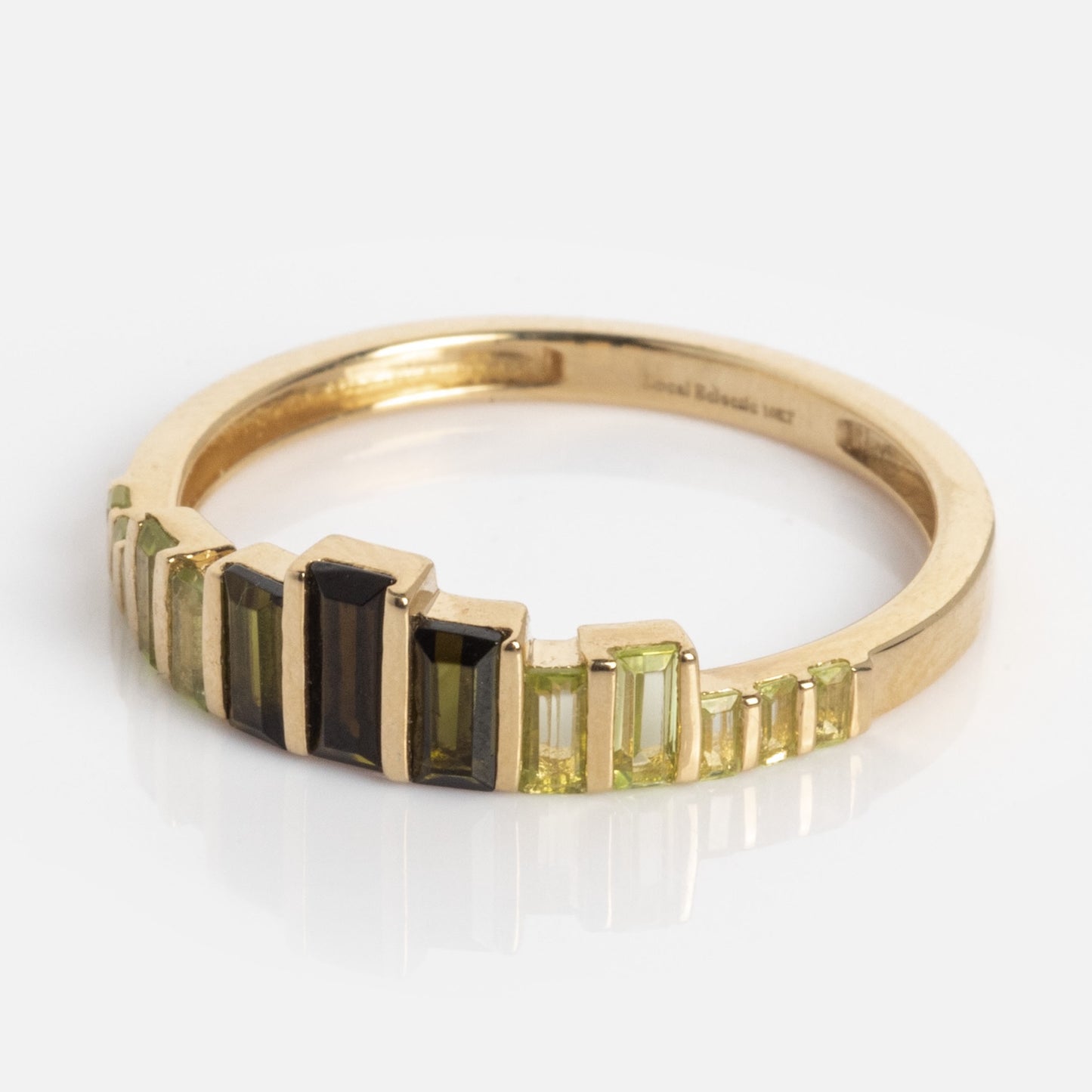 The 10k Green Tourmaline Skyline Band showcases a gold band adorned with baguette-cut green and black tourmalines arranged in a striking, stepped pattern.