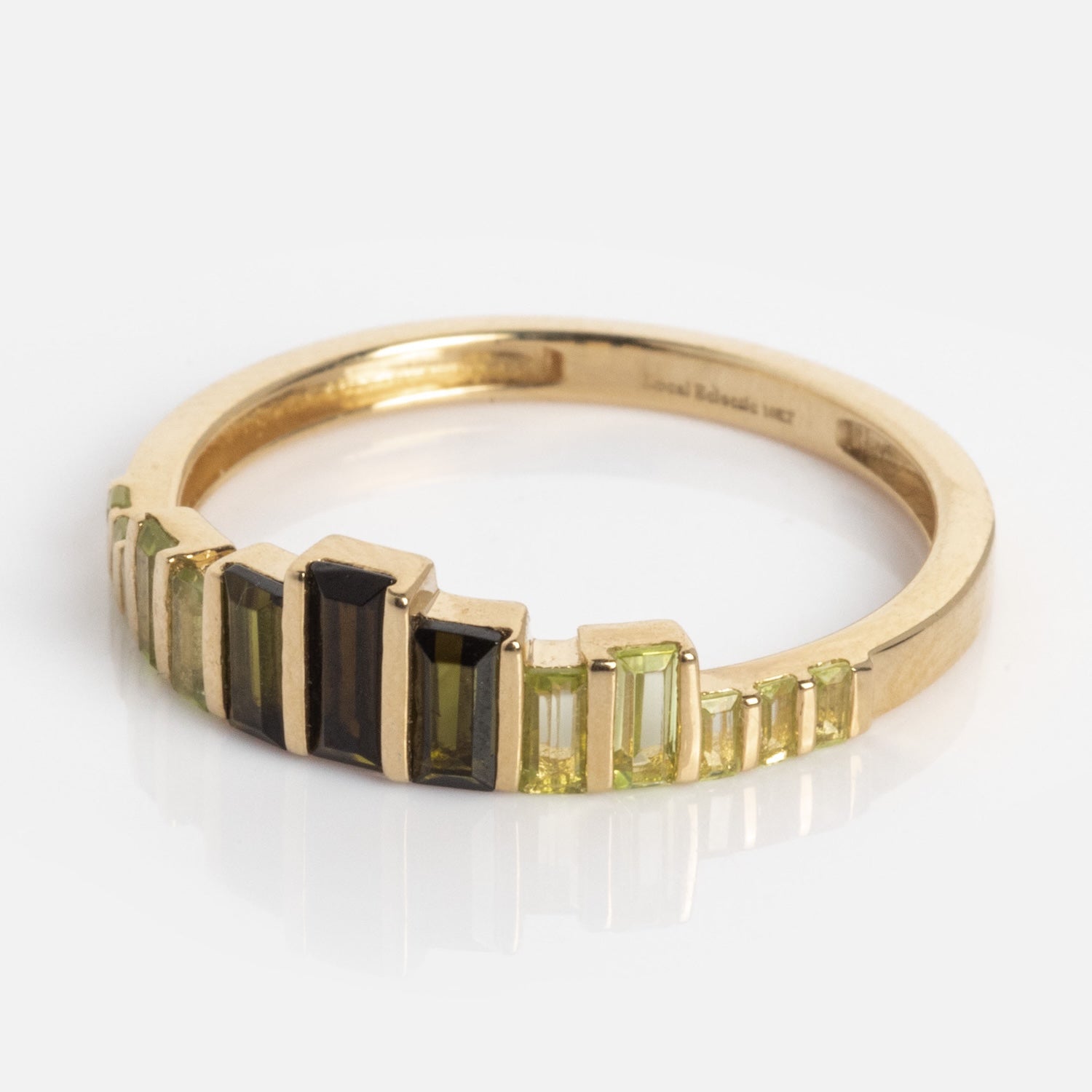 The 10k Green Tourmaline Skyline Band showcases a gold band adorned with baguette-cut green and black tourmalines arranged in a striking, stepped pattern.