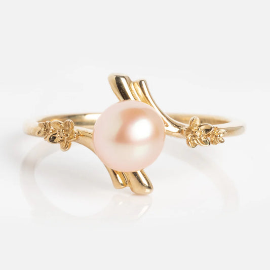 The 10k Forget Me Not Pink Pearl Bypass Ring Size 7 Sample features a delicate gold band with a central round pink pearl and small floral accents, showcased on a plain white background.