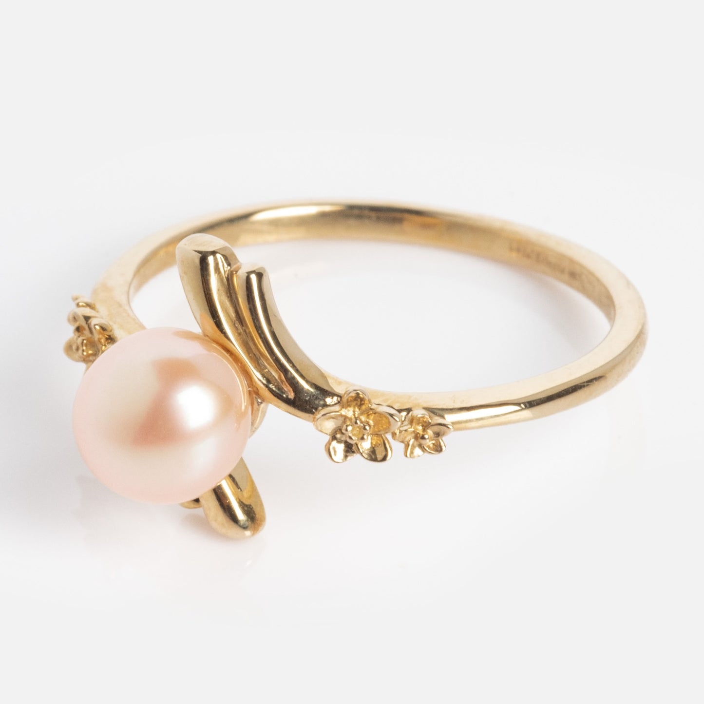 The 10k Forget Me Not Pink Pearl Bypass Ring features a peach-hued pearl and dainty floral accents on the band, set against a white background.
