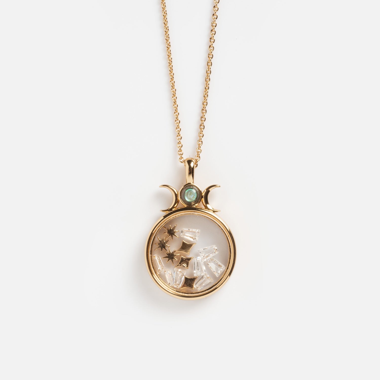 The Wishkeeper Floating Locket Necklace features a gold celestial round glass pendant with a green gemstone, crescent moons, clear crystals, and tiny gold stars inside, displayed on a white background.