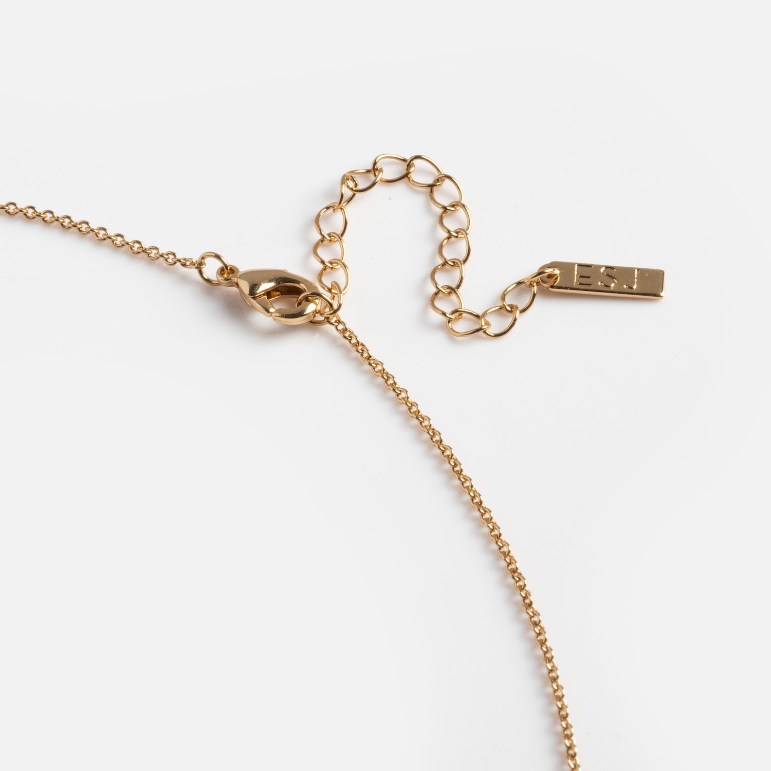 A close-up of the Wishkeeper Floating Locket Necklace, featuring a 14k gold plated chain with a lobster clasp, adjustable extender, and a small rectangular tag at the end.