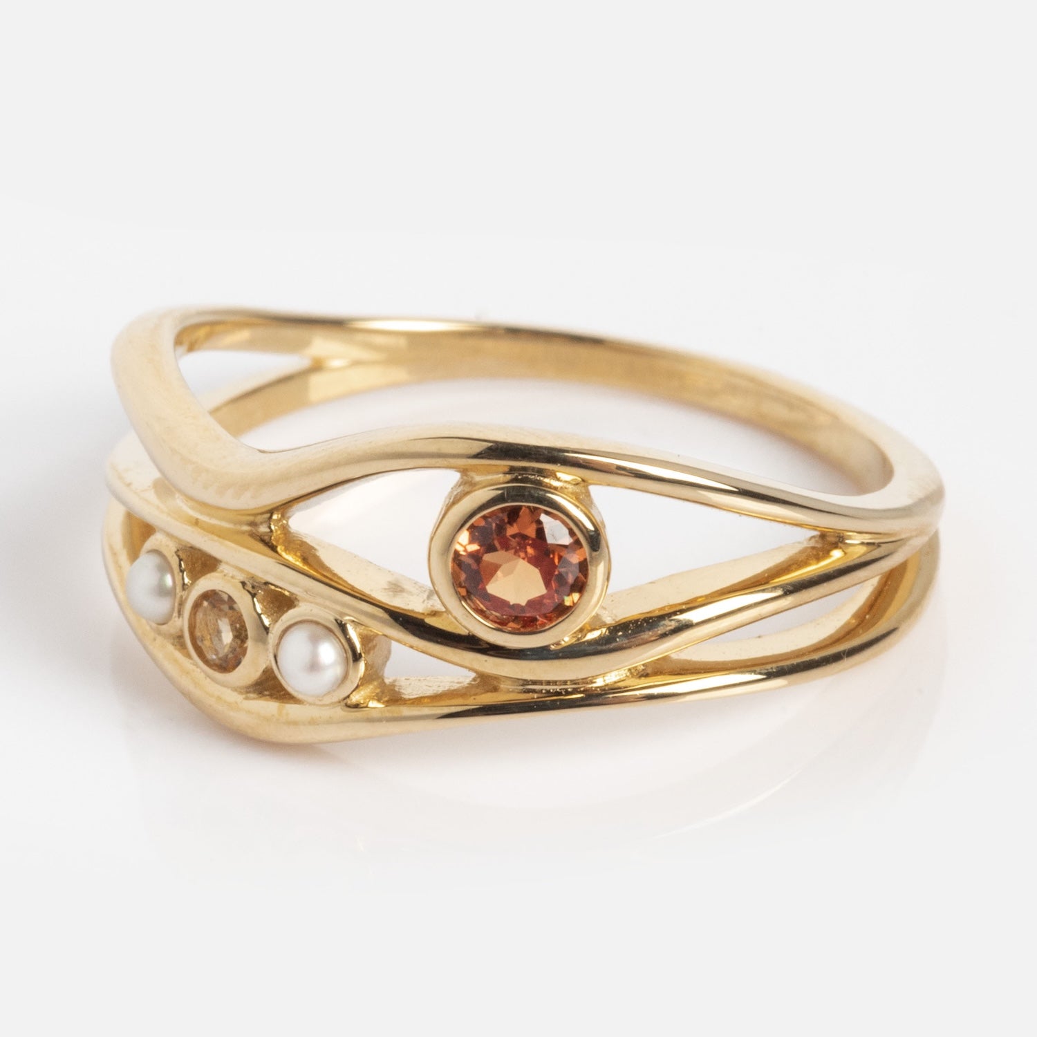 The 10k Orange Sapphire and Citrine Bayside Ring features two overlapping gold bands with a round orange gemstone, two small clear stones, and a pearl set into the modern, delicate design.