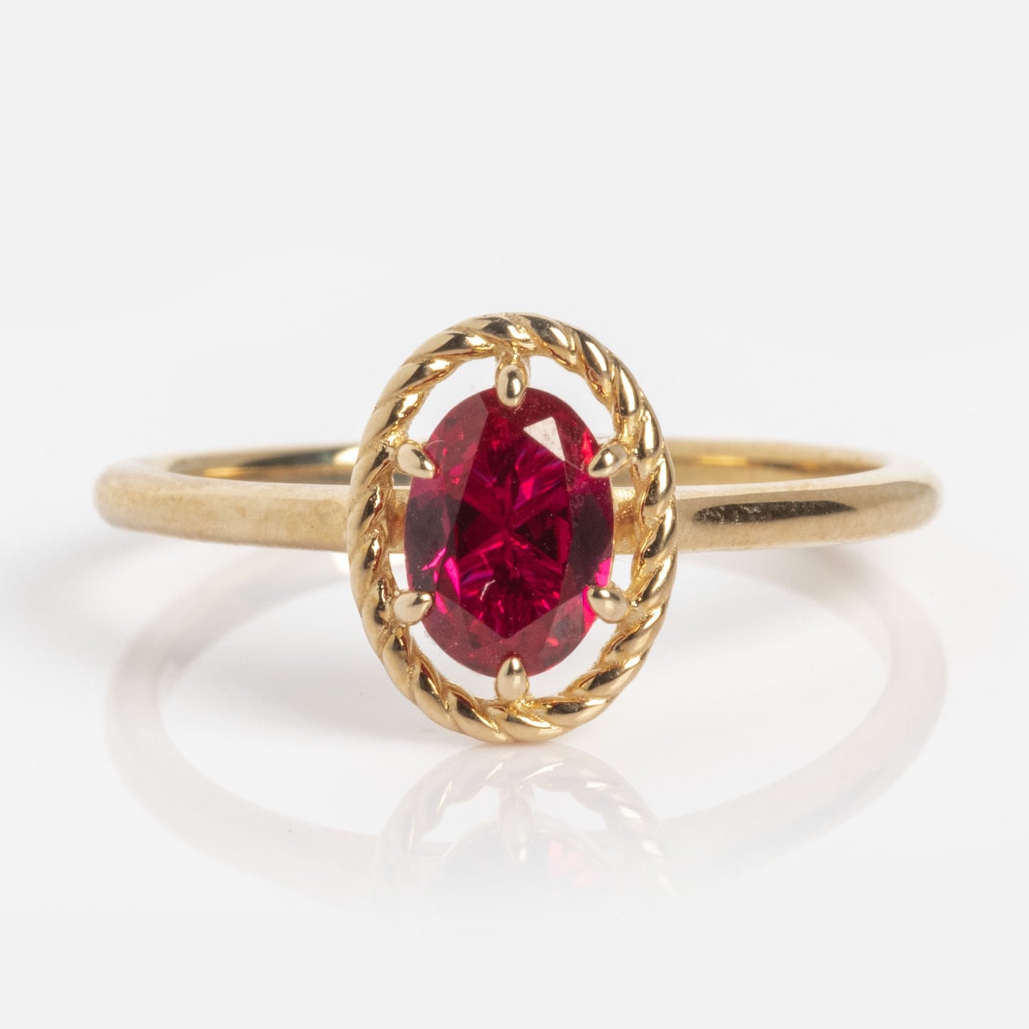 The 10k Lucky In Red Ruby Halo Ring showcases a gold band with an oval-shaped red ruby set in a twisted rope-style bezel, displayed on a plain white background.