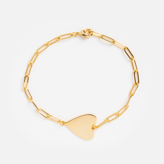 The Amaya Heart Bracelet showcases a gold paperclip chain with elongated oval links and a flat heart-shaped charm, set against a plain white background.