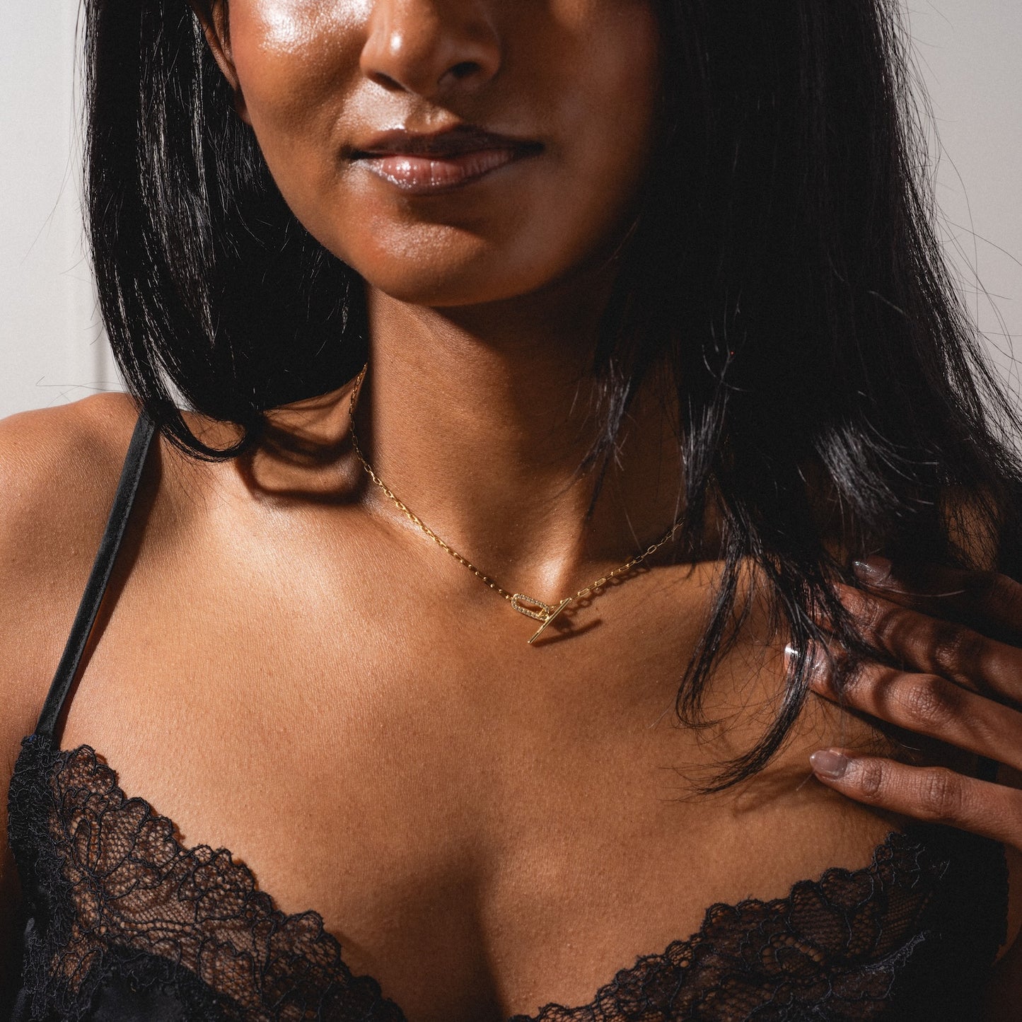 A woman wears a black lace camisole and the Jade Pave Necklace, her hand resting near her collarbone, shown from shoulders to lips.