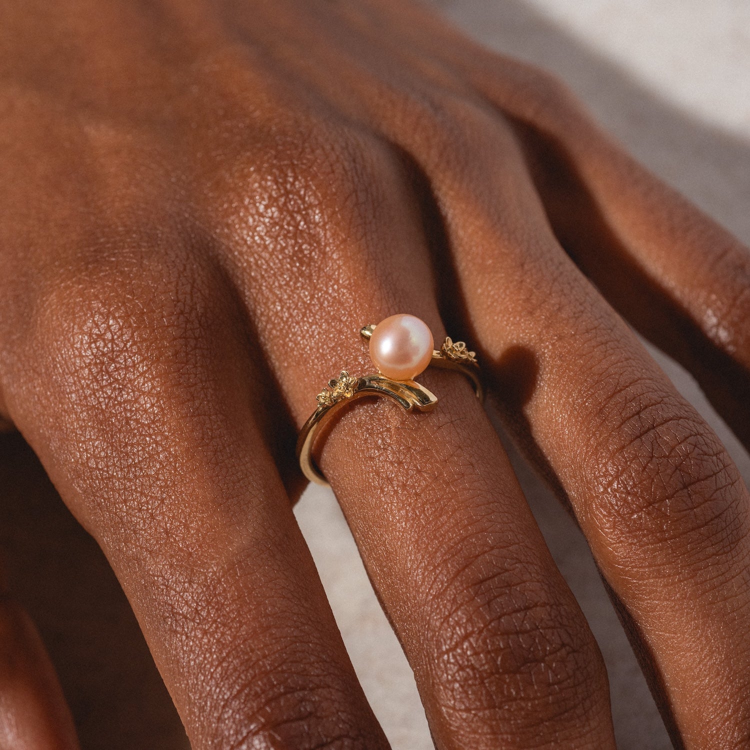 A close-up of a hand wearing the 10k Forget Me Not Pink Pearl Bypass Ring alongside another gold ring with small accents, set against a neutral background.