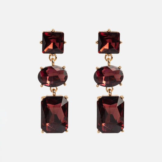 The Allie Earrings are gold drop earrings featuring three faceted red gemstones—square, oval, and rectangular—set vertically against a white background.