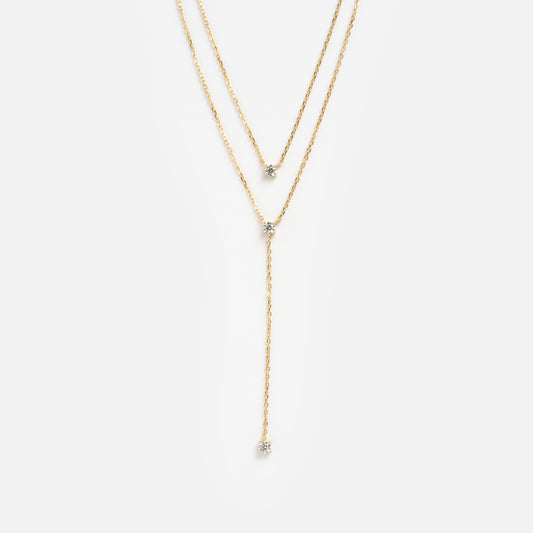 The Solitaire Layered Lariat Necklace features two fine gold chains: one sitting higher, both accented with a single gemstone, and the longer chain finishing in a vertical lariat style with a gemstone drop.
