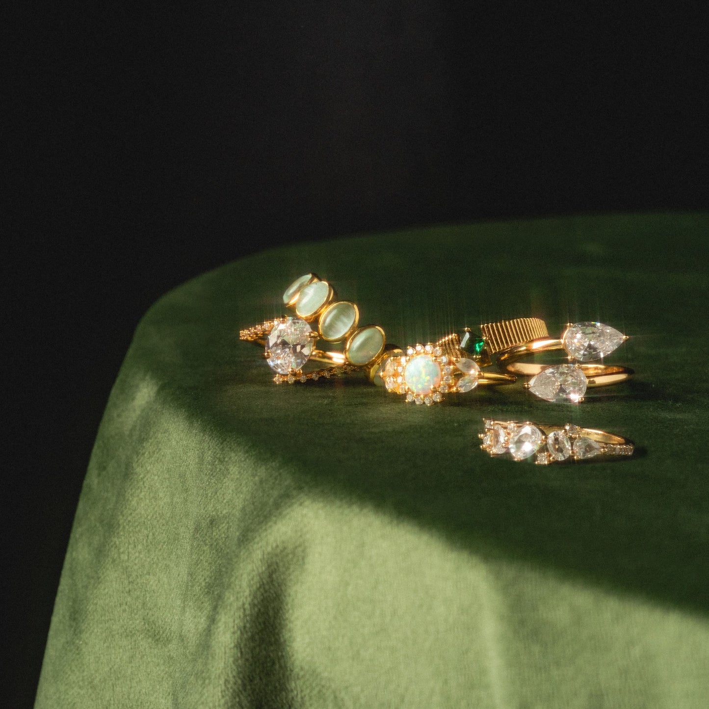 The Tilted CZ Ring is displayed with other gold rings featuring various gemstones and diamond settings on a round, green velvet surface in soft, natural light.
