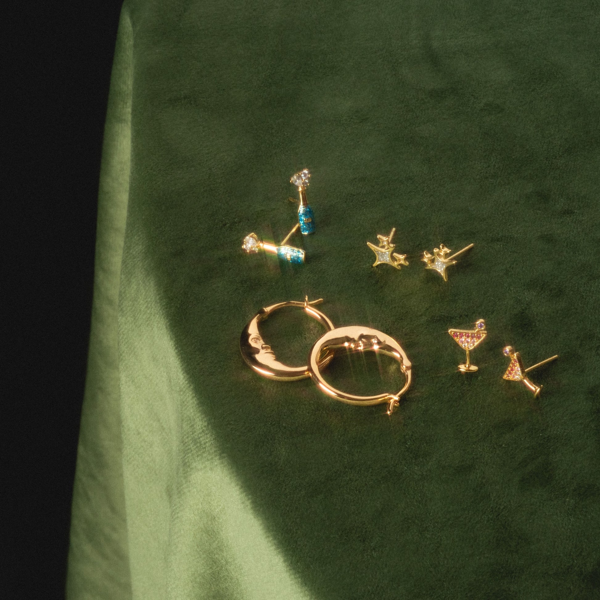 The Twinkling Star Studs, a pair of small gold earrings shaped like stars, are displayed on a green textured fabric surface.