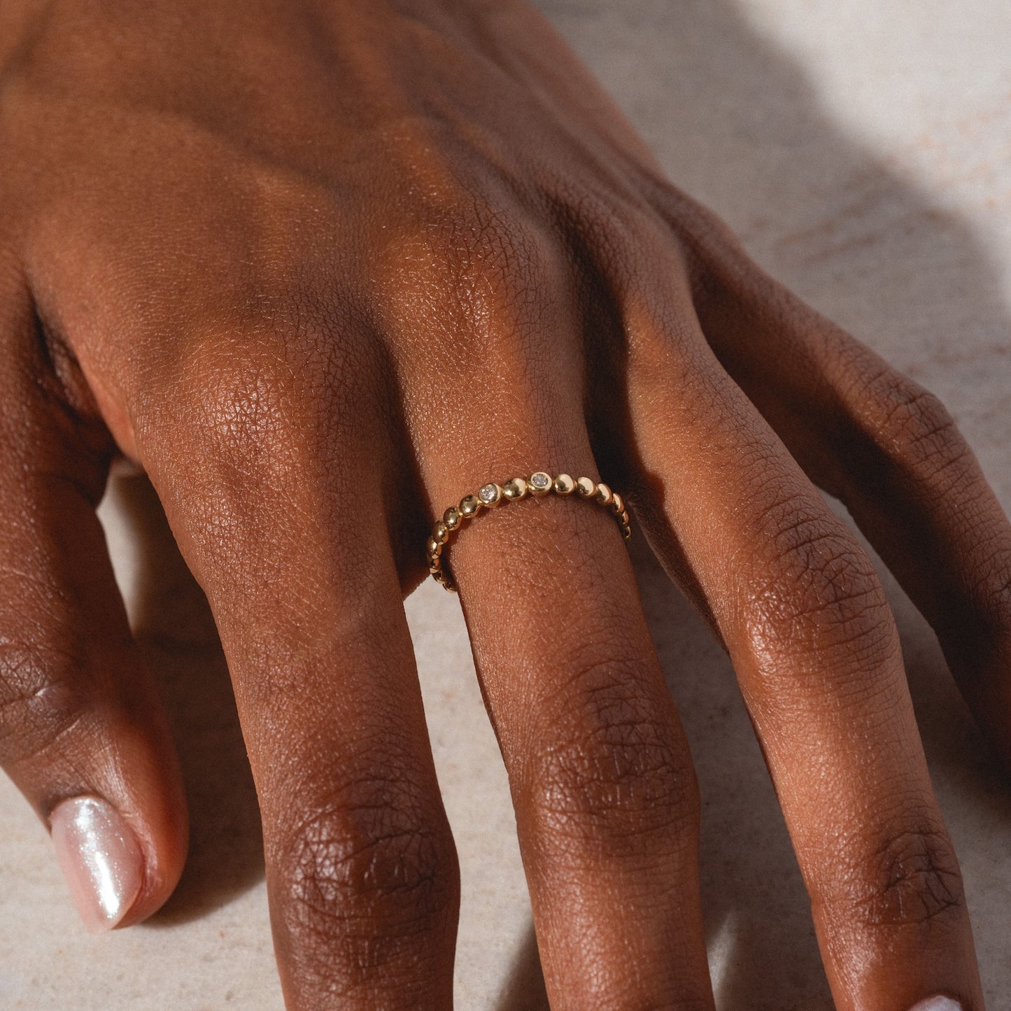 A close-up of a brown-skinned hand wearing the 10k Hidden Message Morse Code Diamond Band on the middle finger, resting on a light surface. The natural nails have a slight sheen.