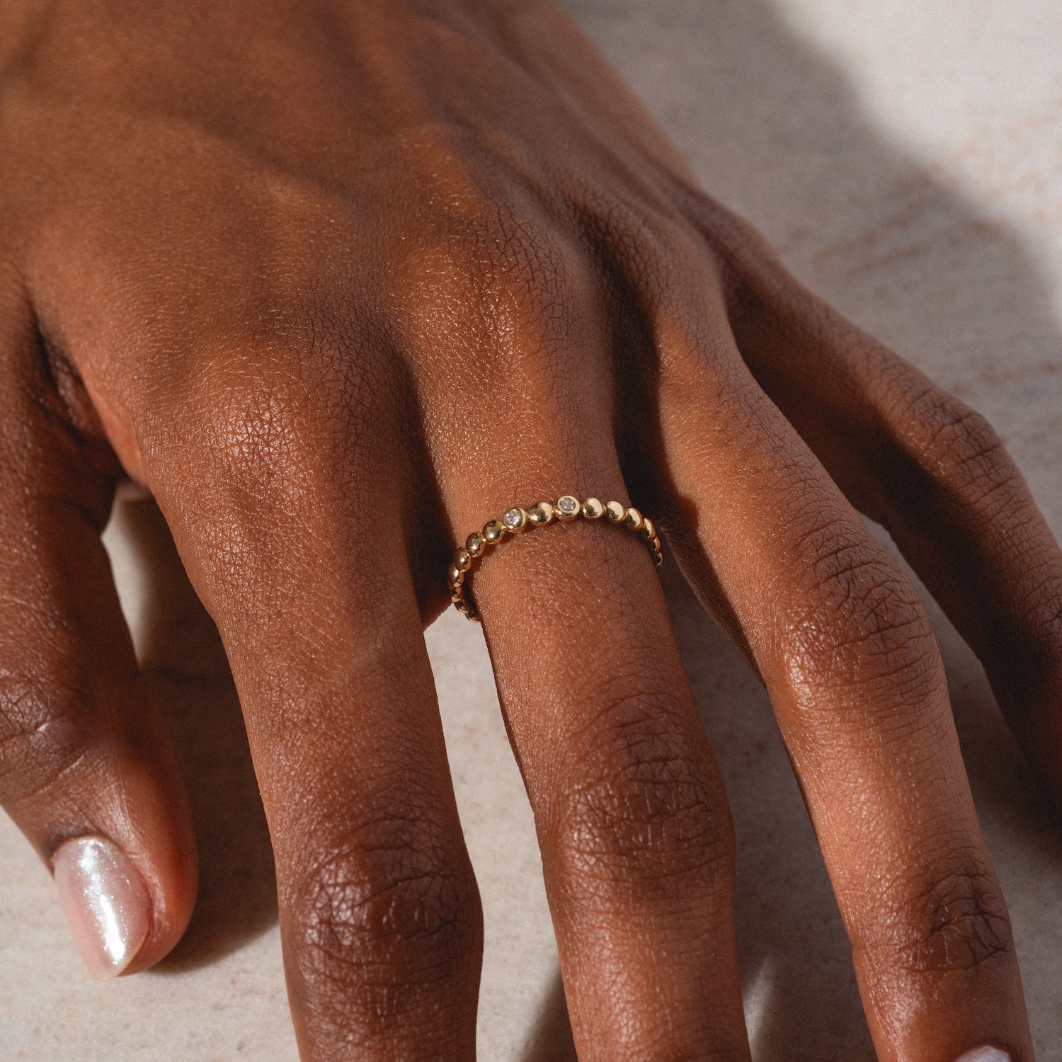 A close-up of a brown-skinned hand wearing the 10k Hidden Message Morse Code Diamond Band on the middle finger, resting on a light surface. The natural nails have a slight sheen.