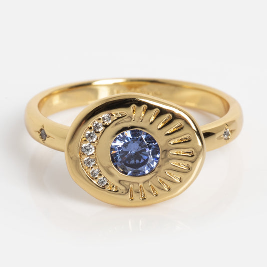 The Eternal Bond Sun and Moon Ring is a gold ring with a central round blue gemstone, engraved rays, a crescent adorned with white stones, and additional tiny stones set on the band’s sides.