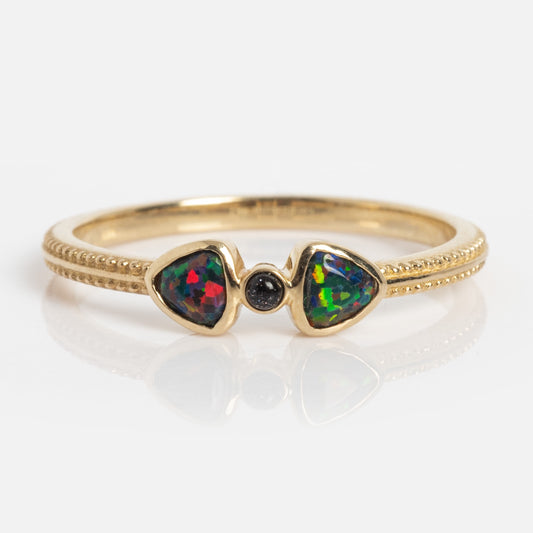 The Solid Gold Black Opal Divine Direction Ring features a gold beaded band with two triangular opals flanking a small round black gemstone, all elegantly set in solid gold.