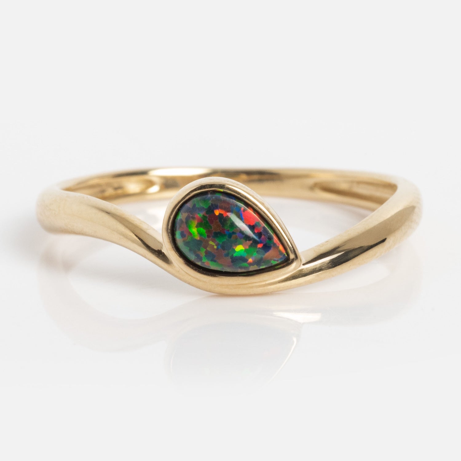 The Solid Gold Black Opal Galaxy Droplet Ring showcases a teardrop-shaped opal with vivid green, blue, and red hues, set in a smooth curved gold band and displayed on a white background.