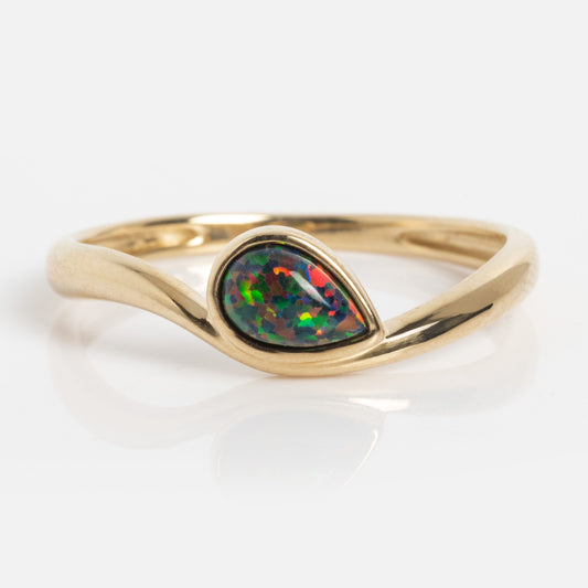 The Solid Gold Black Opal Galaxy Droplet Ring showcases a teardrop-shaped opal with vivid green, blue, and red hues, set in a smooth curved gold band and displayed on a white background.