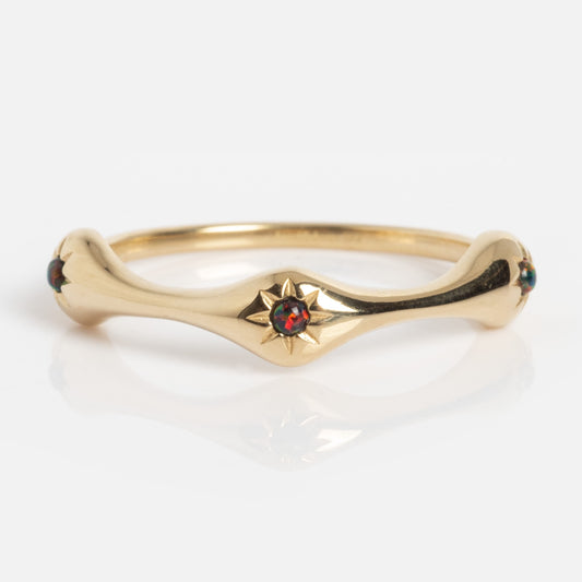 The Solid Gold Black Opal Stars Aligned Ring features a star-shaped setting with a vibrant black opal at its center and small accent stones on each side. The curved gold band is showcased against a white background.