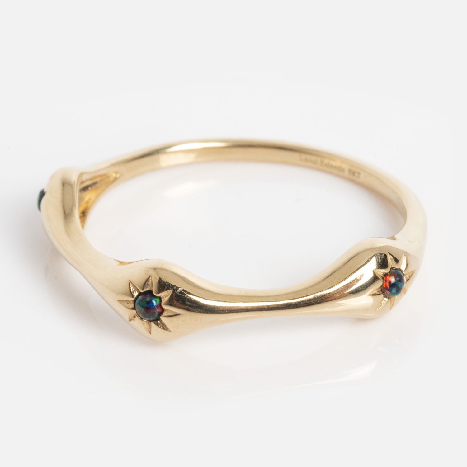 A thin Solid Gold Black Opal Stars Aligned Ring with a gentle wave design, featuring small round black opals set in star-shaped settings along the band. The background is plain white.