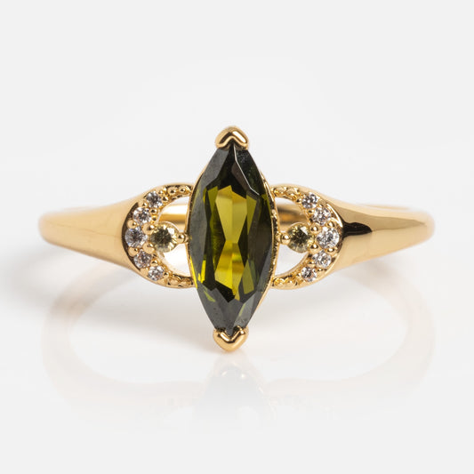 The Witching Hour Crescent Moon Ring is a gold ring with a marquise-cut green gemstone at the center, accented by crescent moon-shaped arcs adorned with small clear stones, shown on a plain white background.